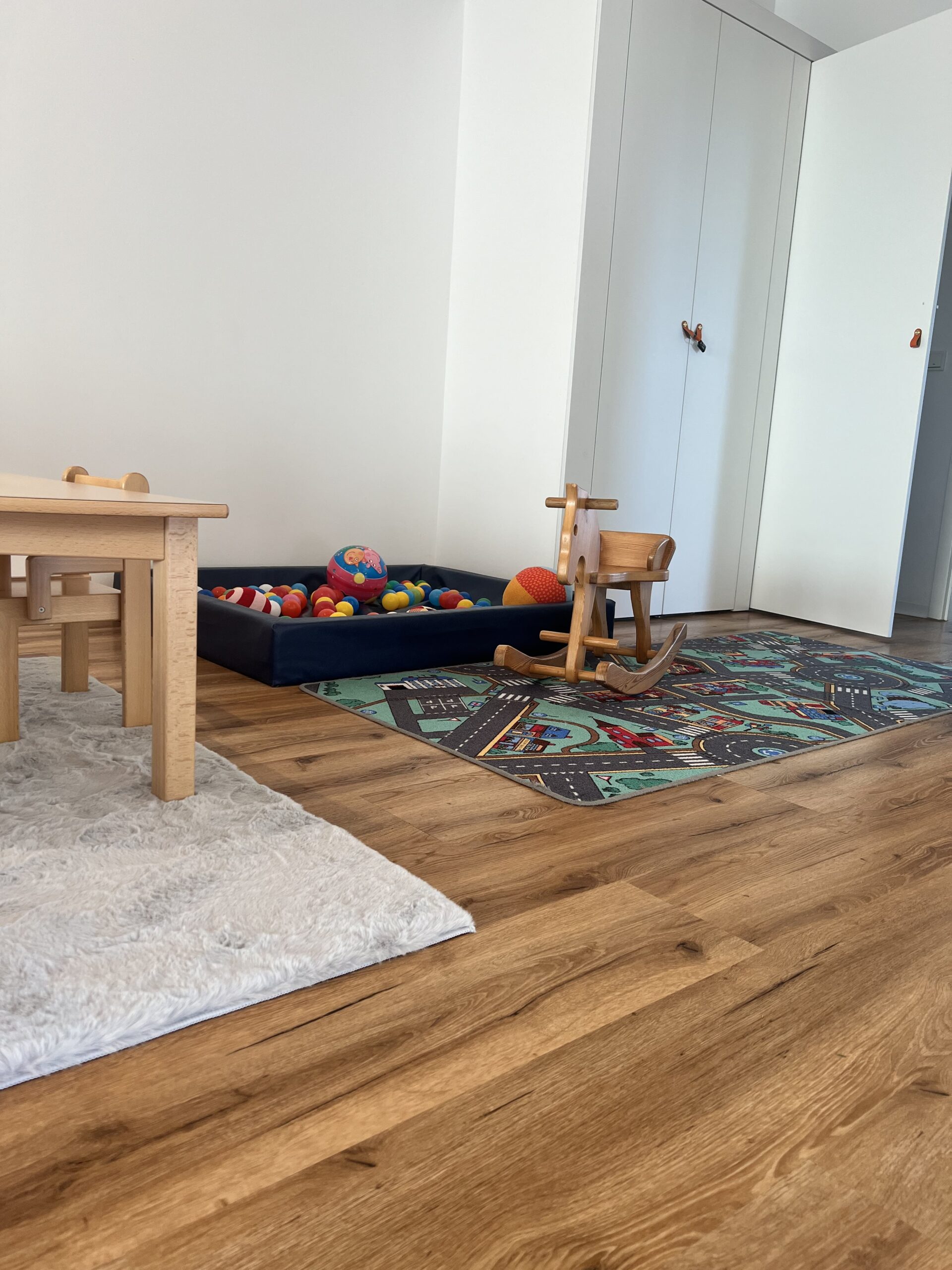 Spielecke mit Bällebad, Schaukelpferd und Straßenteppich auf hellem Holzfußboden.