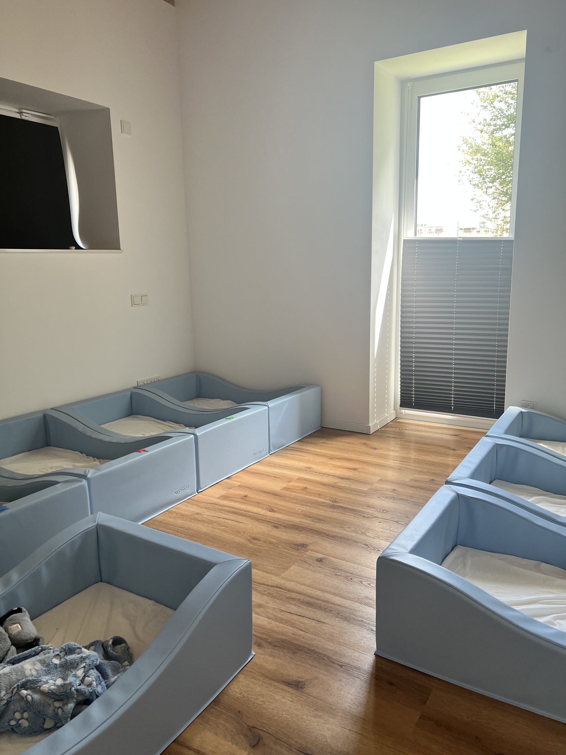 Ruhiger Raum mit mehreren weichen Kinderbetten in Hellblau, ideal für die Mittagsruhe.