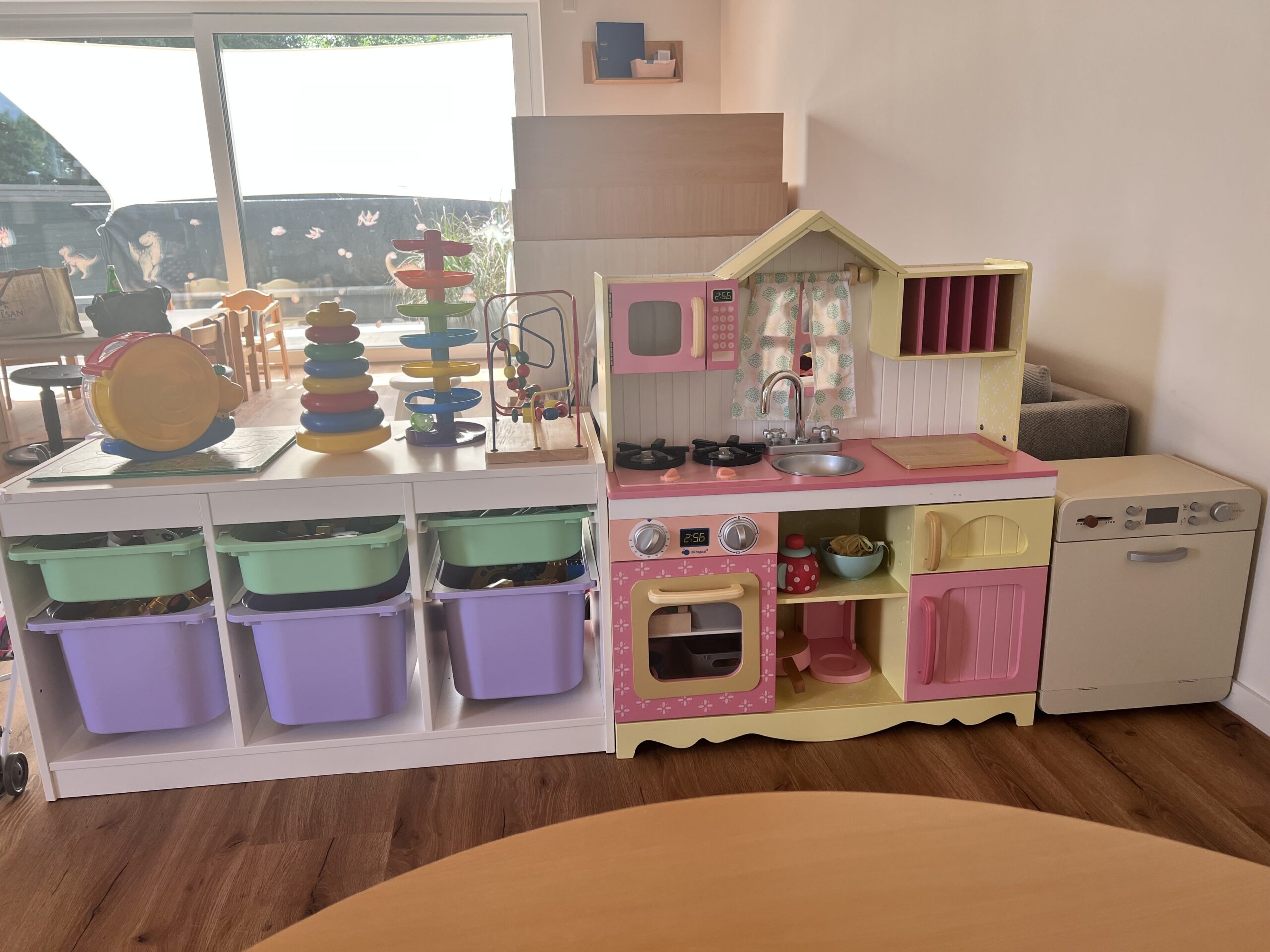 Detailaufnahme einer Spielküche in Rosa-Gelb, daneben ein Regal mit bunten Spielzeugboxen und Motorikspielzeug.